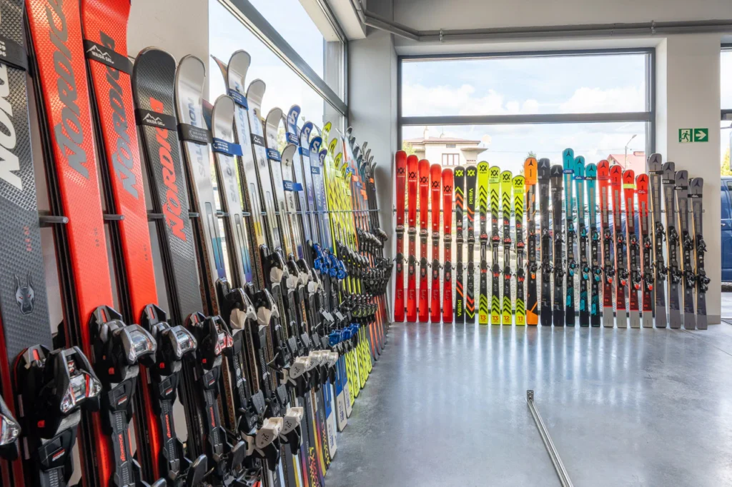 Kolorowe narty są starannie ustawione w rzędach i wyeksponowane pionowo na ścianach jasnego, nowoczesnego sklepu z nartami Wajda-Ski w Rzeszowie, z dużymi oknami wpuszczającymi naturalne światło - prezentacja zdjęć nieruchomości.