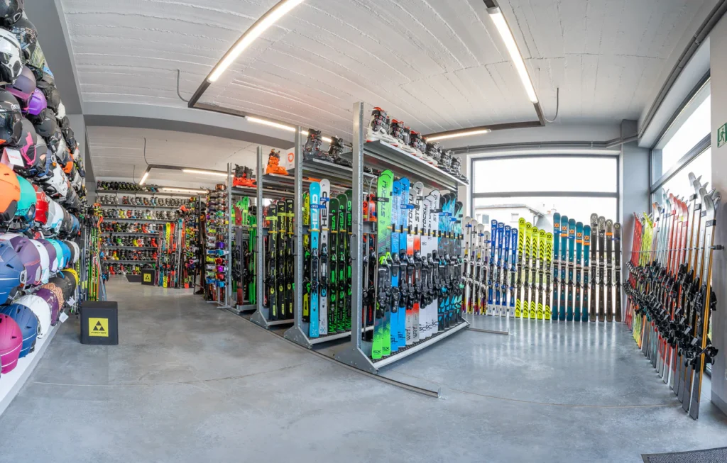 Dobrze oświetlone wnętrze sklepu narciarskiego w Rzeszowie, z rzędami kolorowych nart, desek snowboardowych, butów i kasków uporządkowanych na półkach i wieszakach. Duże okna wypełniają przestrzeń naturalnym światłem. Zdjęcia wnętrz idealnie oddają żywy układ.