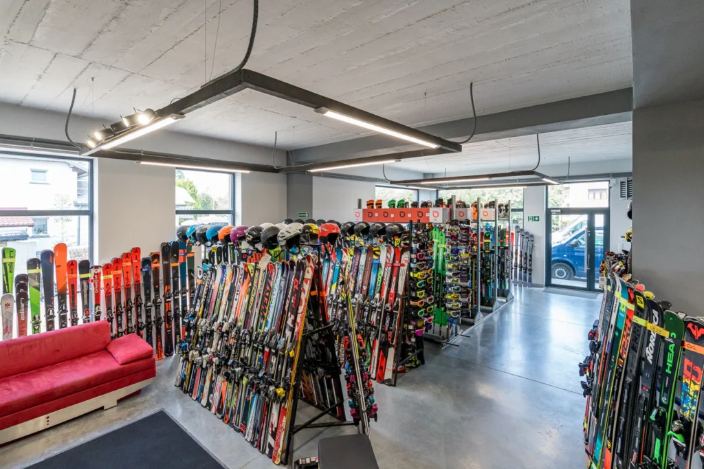 Wajda-Ski - nowoczesny sklep narciarski. Duże okna wypełniają przestrzeń światłem, podkreślając czerwoną kanapę na polerowanej betonowej podłodze - tak powinny wyglądać zdjęcia wewnątrz sklepu!