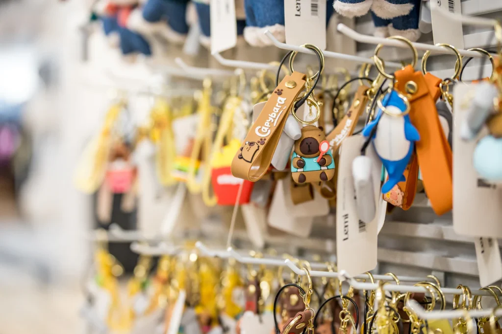 Stojak wypełniony kolorowymi breloczkami, w tym brązowym misiem i paskiem "Care Bear", wszystkie wiszące na hakach w sklepie - zachęcająca scena uchwycona na profesjonalnym zdjęciu podczas otwarcia sklepu Rzeszów.